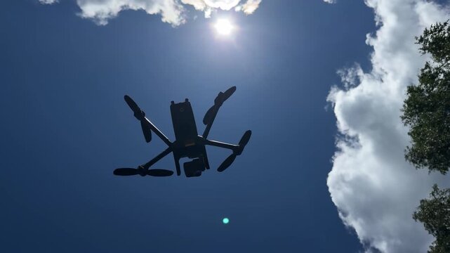 Low angle view of a professional quadcopter drone with rotating propellers flying high in the clear blue sky