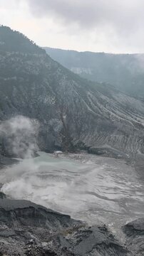 Breathtaking panoramic view of the Tangkuban Perahu active volcano crater in West Java, Indonesia, with sulfur smoke rising from the green geo-thermal lake.
