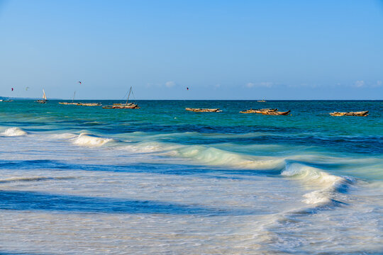 Traditional wooden fishing boat dhows at Zanzibar island, Tanzania. Kitesurfers on background