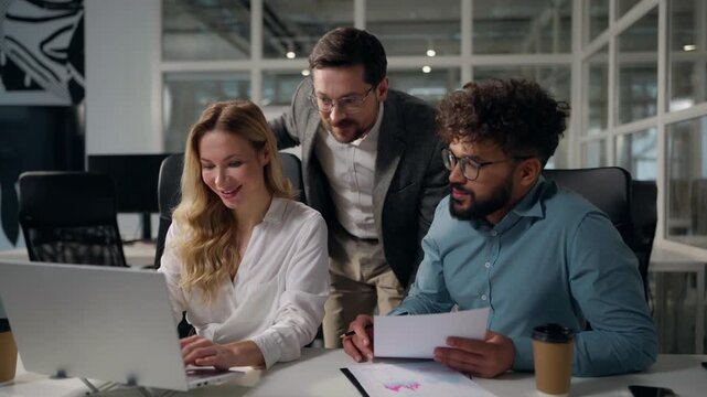 Three happy excited multiethnic business workers working with laptop documents talking in office boss rejoice good work diversity managers excellent result financial growth corporate team talk smile