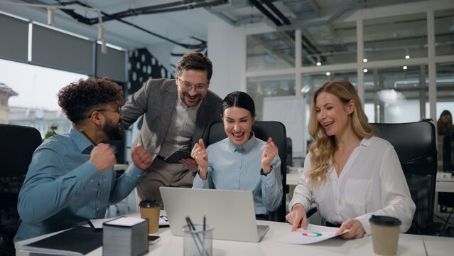 Four multiethnic business people working together with laptop talking winning job success giving high five celebrating multiracial businessmen and businesswomen colleagues win achieve team in office