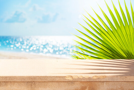 Stone table for placing product overlooking blurred seascape with tropical beach landscape and green palm leaves