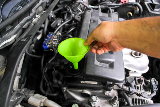 Hand holding a bright green plastic funnel over a car engine oil filler hole, preparing for a routine engine oil change