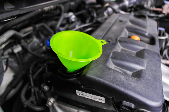 Bright green plastic funnel placed in a car engine oil filler hole, ready for a routine oil change and automotive maintenance