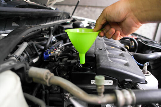 Hand holding a bright green plastic funnel over a car engine oil filler hole, preparing for a routine engine oil change