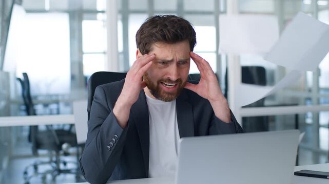 Stressed Caucasian mature business man feeling headache looking in laptop flying papers documents around overload middle-aged businessman male look in computer feel tired in office failed work problem