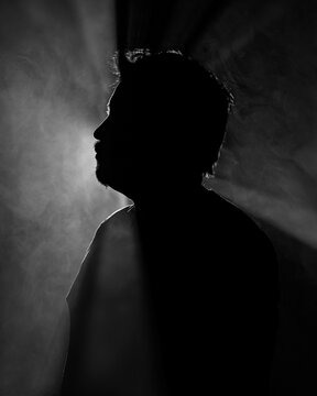 Dramatic black and white profile silhouette of man in smoke with light beams evoking mystery, inner thoughts, and creative identity for advertising.