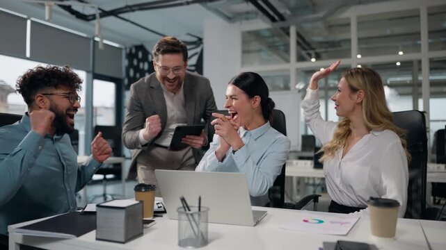 Four multiethnic business people win at meeting with laptop celebrate success work giving high five working talking happy team conference briefing colleagues winning in office trading financial growth