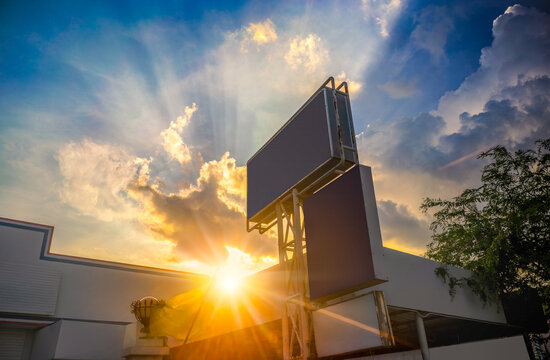 Low angle view of empty blank billboard advertising sign against dramatic sunset sky with golden sunbeams rays and blue cloudy sky. Perfect copy space for text, advertisement, and marketing concepts. 