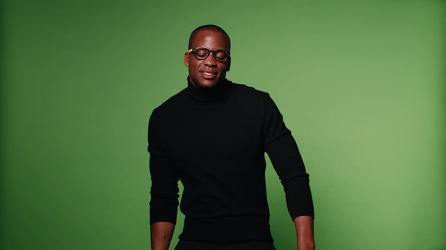A stylish African-American man in a black turtleneck and glasses moves rhythmically on a green screen background. Perfect for a variety of creative projects.