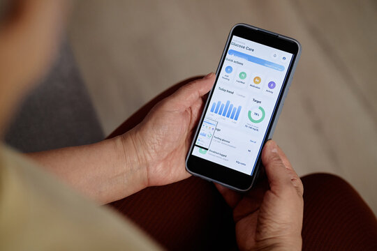 Close up of woman holding smartphone, monitoring glucose data in health app for diabetes self management and preventive care. Ideal for telehealth, wellness, mobile health marketing