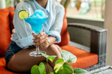Obraz premium Young asian woman drinking a frozen blue margarita cocktail in outdoors tropical garden bar in bali