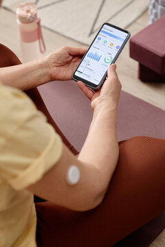 Vertical shot of  woman checking glucose monitoring app on smartphone, wearing sensor patch on arm. Useful for diabetes management, digital health, telemedicine marketing