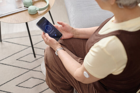 Senior woman holding smartphone and monitoring health data at home, showing digital self care and chronic condition management. Useful for telehealth, wellness app, remote care marketing