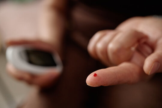 Close up of woman pricking finger and checking blood sugar with glucose meter, showing diabetes self monitoring. Useful for healthcare campaigns, prevention content