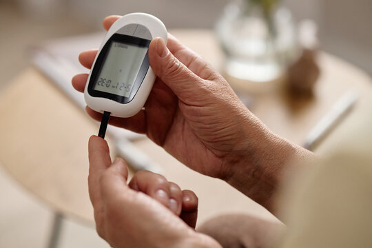Close up of woman inserting test strip into blood glucose meter, checking diabetes level for home monitoring. Ideal for healthcare, chronic disease management, prevention