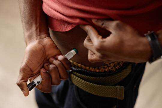 Close up of Black man injecting abdomen with insulin pen, managing diabetes through self care and home treatment. Ideal for healthcare campaigns, chronic illness education, medical support