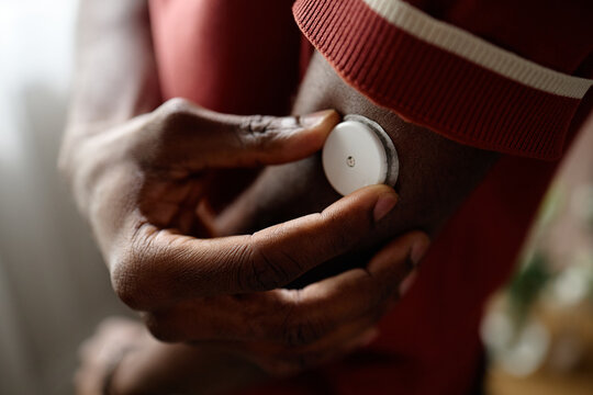 Close up of Black adult applying wearable health sensor on arm, monitoring glucose or wellness data for chronic care management. Useful for medical technology, telehealth, insurance campaigns