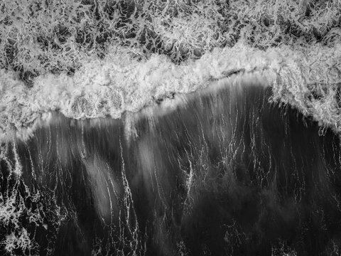 Aerial view of powerful crashing waves and white sea foam against dark ocean water in black and white Albany, Western Australia, Australia.