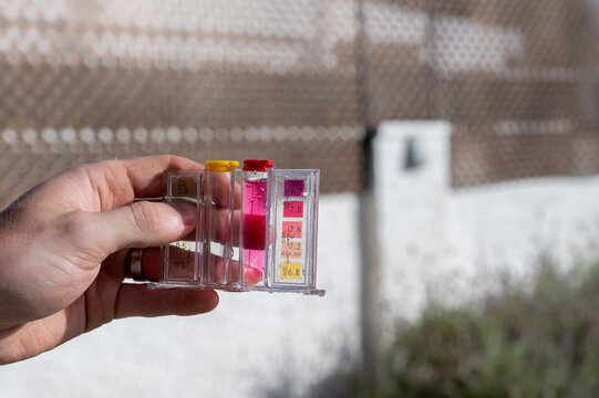 Mano sosteniendo un medidor qu&iacute;mico para comprobar el pH y cloro del agua de una piscina antes de aplicar productos de ajuste.