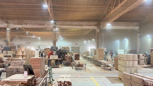 Woodworking factory interior with workers and stacks of lumber on tables and floor
