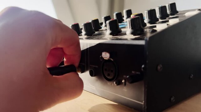 Close-up of a hand unplugging a jack cable from a broadcast intercom unit, with audio socket, XLR connector, control knobs, and live production gear.