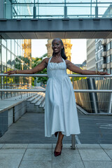 Fototapeta premium Woman stands on a railing wearing a white dress at a modern city location during sunset