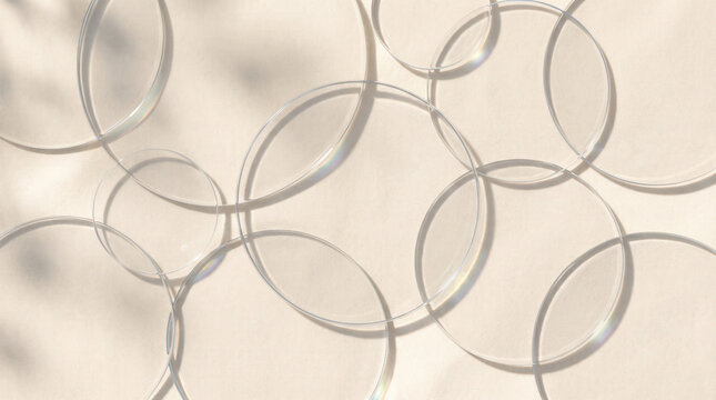 Top down abstract arrangement of overlapping transparent glass circles casting soft shadows on beige surface suggesting minimal pattern texture optical design calm modern background