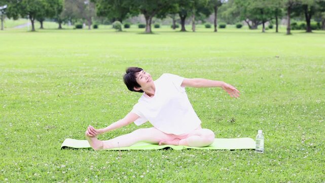 公園でヨガの側屈ストレッチをする笑顔のアクティブシニア女性