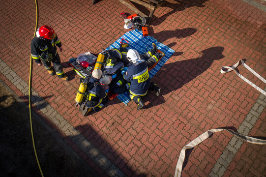 Aerial view of firefighters in uniform performing a rescue exercise on a red brick pavement with equipment and hoses in Debrzno, Pomeranian Voivodeship, Poland.