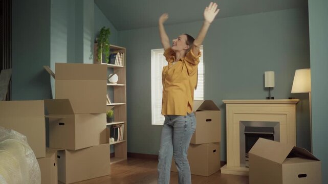 Joyful woman spinning around and dancing happily among cardboard boxes after moving into her brand new home, celebrating a successful relocation and the beginning of a new chapter in her life