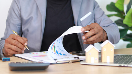 Real estate agent reviewing property investment reports and housing market data at office desk with...