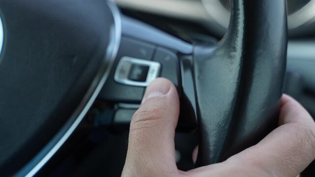 Driver Pressing Steering Wheel Control Button in Modern Car