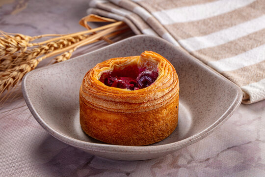 Gourmet cruffin pastry, berry fruit filling, ceramic bowl, rustic setting, wheat stalks, striped towel