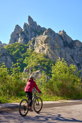 Fototapeta premium Active senior woman riding an electric mountain bike on a scenic road in the Lucanian Dolomites near Castelmezzano, Basilicata, Italy. Outdoor adventure, sustainable travel, fitness, and nature 