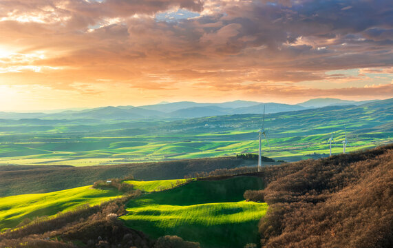 green valley with nice farmland fieds and hills with wind turbines on agricultural landscape. Beautiful rural landscape with cloudy sky on background