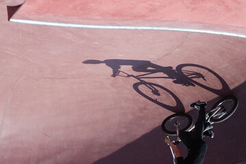 Naklejka premium A creative perspective shot showing the shadow of a cyclist on a red skate park bowl surface, with the rider visible in the corner.