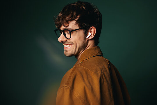 Casual business man with glasses and earbuds smiles in studio profile