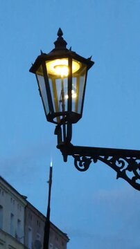 Historic Wroclaw gas street lamp glowing with warm orange light during twilight, iconic traditional lantern at Ostrow Tumski with a lamplighter pole visible against a moody blue evening sky