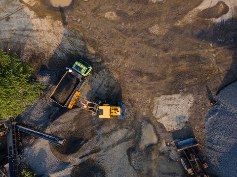 Aerial view of the Babakan construction site with an excavator loading a truck and piles of gravel in Karanglewas, Central Java, Indonesia.
