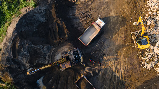 Aerial view of excavators and dump trucks working at the Babakan construction site with workers and piles of earth in Karanglewas, Central Java, Indonesia.