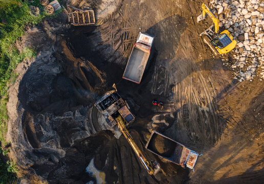 Aerial view of heavy machinery including excavators and dump trucks working at a construction site with piles of rocks in Karanglewas, Central Java, Indonesia.