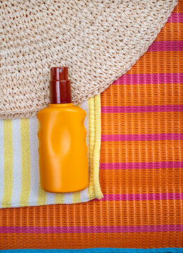 Sunscreen spf spray and straw hat on orange stripped background