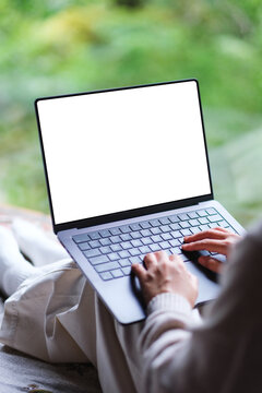Vertical mockup image of a woman working on laptop computer with blank desktop white screen on the bed at home