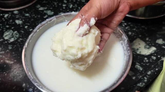 Close up of a hand lifting freshly churned Bilona makkhan from cultured milk, showcasing the creamy texture, traditional dairy preparation process, and authentic homemade butter in an Indian kitchen