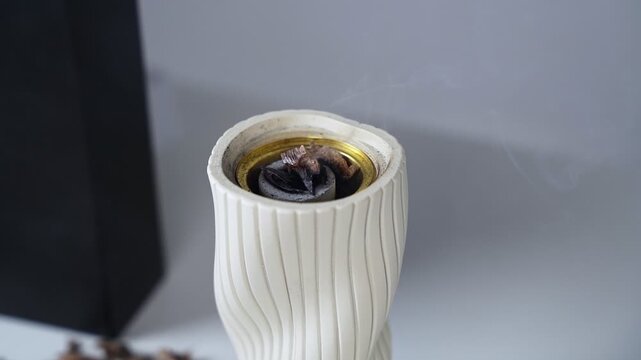 shot of traditional Arabic oud burning on charcoal inside an elegant white ceramic mabkhara. Fragrant smoke slowly rises against a clean, softly lit indoor studio background.