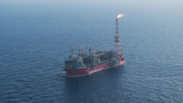 Aerial view of an FPSO floating production storage and offloading vessel operating at sea with a bright orange flare burning from the gas tower.