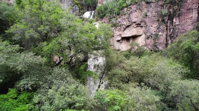 Aerial drone footage revealing a waterfall flowing through rocky cliffs and lush vegetation in Cerro Blanco, Aguascalientes, Mexico. Scenic natural landscape surrounded by greenery and rugged terrain.