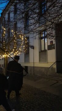 Traditional lamplighter in black cape walking down cobblestone streets at twilight to light gas lamps in Ostrow Tumski, Wroclaw, Poland, cultural lifestyle travel video clip