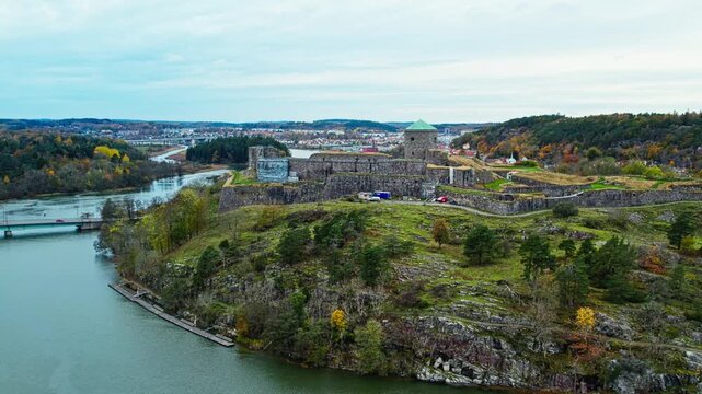 Aerial drone view of historic Bohus Fortress surrounded by autumn colors overlooking river and surrounding town with stone walls rugged terrain and scenic landscape